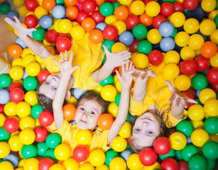 Fototapeta na wymiar Three happy little kids girls in ball pit smiling happily at camera while having fun in children play center. Top view