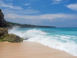 Turquoise waves crash against stones with splashes. Bali.