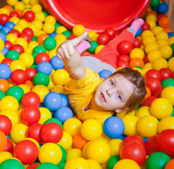 Fototapeta na wymiar Happy little girl playing and having fun at kindergarten with colorful balls and show thumb up in play center