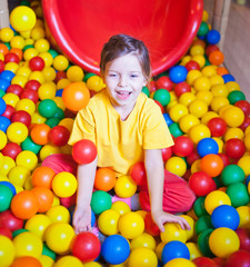 Fototapeta na wymiar Happy little girl playing in colorful balls. Happy child playing at colorful plastic balls in play center