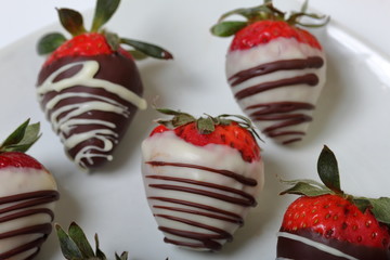 Strawberries glazed in black and white chocolate. Lie on a white plate with a pattern.