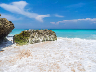 Turquoise waves crash against stones with splashes. Bali.