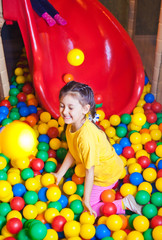 Fototapeta na wymiar Happy little girl playing in colorful balls. Happy child playing at colorful plastic balls in play center