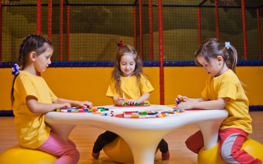 Three happy little girls playing with toy bricks on the table in kindergarten