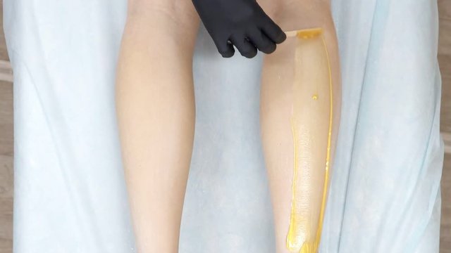 beautician applies wax on women's legs for hair removal.