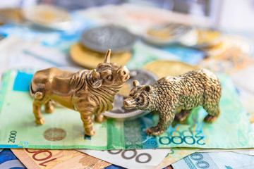 Bronze figures of a bull and a bear on the background of paper money and metal coins. Blur...