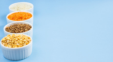 Assorted different cereals on a blue background. Buckwheat, lentils, rice, peas in plates on top, copy of the place. Healthy eating concept