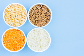 Assorted different cereals on a blue background. Buckwheat, lentils, rice, peas in plates top view, copy space