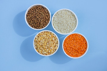 Assorted different cereals on a blue background. Buckwheat, lentils, rice, peas in plates top view, copy space