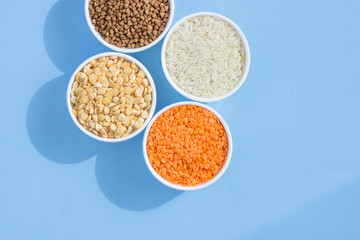 Assorted different cereals on a blue background. Buckwheat, lentils, rice, peas in plates top view, copy space