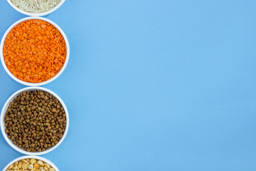 Assorted different cereals on a blue background. Buckwheat, lentils, rice, peas in plates top view, copy space
