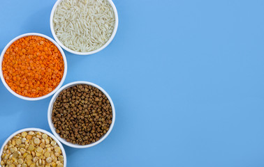 Assorted different cereals on a blue background. Buckwheat, lentils, rice, peas in plates top view, copy space