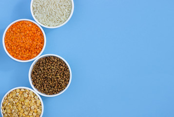 Assorted different cereals on a blue background. Buckwheat, lentils, rice, peas in plates top view, copy space
