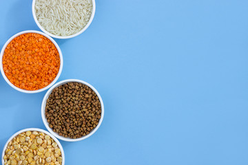 Assorted different cereals on a blue background. Buckwheat, lentils, rice, peas in plates top view, copy space