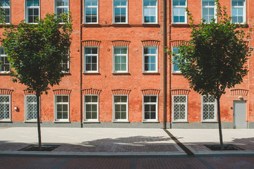 Fototapeta na wymiar Office building in loft style. Large Windows. Red brick wall. Green bushes on the middle. Flat fasade composition