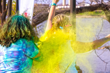 Fototapeta na wymiar Girl with arms up gets coated with yellow powder at Holi Color Festival - selective focus - unrecognizable people - bright colors