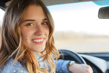 Back view of attractive woman in car, sitting at wheel, turning and looking at passengers in back seat. Beautiful female looks at camera with toothy smile, being glad to pass exam in driving school.