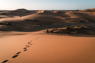 Fototapeta na wymiar Man walks in the dunes of the Moroccan Sahara desert