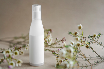 Obraz na płótnie Canvas White cosmetic bottle on beige background decorated with white flowers