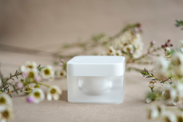 Fototapeta na wymiar White square cosmetic jar on a beige background decorated with white flowers