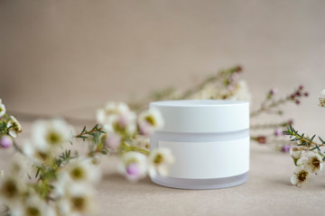 Fototapeta na wymiar White round cosmetic jar on a beige background decorated with white flowers