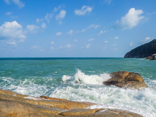 Turquoise waves crash against stones with splashes. Thailand.