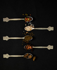Kitchen concept: spices on spoons, top view, black background, selective focus