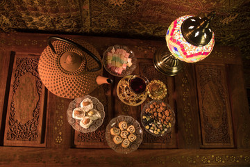 Arabian tea in glass with eastern snacks on vintage wooden surface. Eastern tea concept. Low light lounge interior with carpet. Empty space.
