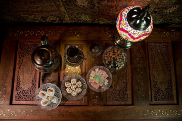 Fototapeta na wymiar Arabian tea in glass with eastern snacks on vintage wooden surface. Eastern tea concept. Low light lounge interior with carpet. Empty space.