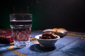 Water and dates. Iftar is the evening meal. View of decoration Ramadan Kareem holiday on carpet. Festive greeting card, invitation for Muslim holy month Ramadan Kareem. Dark background
