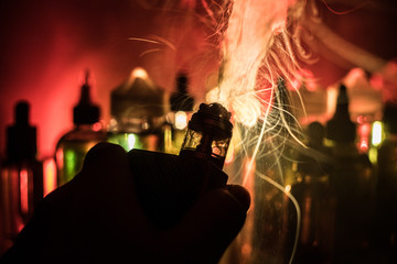 Vape concept. Electronic Cigarette vape explosion. Smoke clouds and vape liquid bottles on dark...
