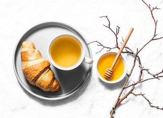 Tea time. Green tea with honey and croissant on a light background, top view