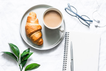 Morning plan. Coffee, croissant and a clean empty notebook on a light background, top view. Flat lay, copy space
