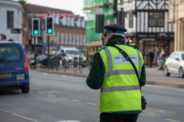 civil enforcement officer or traffic warden walks up the street whilst writing a parking ticket in the UK