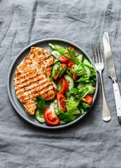Grilled turkey chops and tomatoes, cucumbers, greens salad on a gray background, top view. Healthy food diet concept