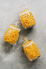 Flat lay a variety of pasta in glass jars on a gray background. View from above.