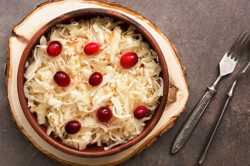 A bowl of sauerkraut with cranberries on a wooden stump, rustic brown background. Top view, flat lay.