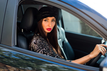 fashionable stylish lady sits behind the wheel of a car, drives along the road, smiles, looks into the camera, transport, woman behind the wheel