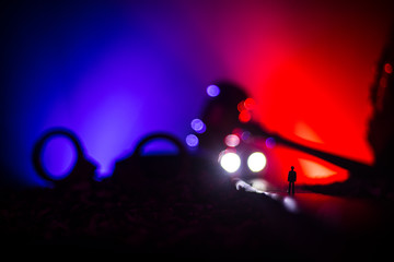 Fototapeta na wymiar Legal law concept. Silhouette of handcuffs with The Statue of Justice on backside with the flashing red and blue police lights at foggy background. Selective focus