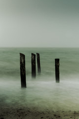 Wooden pillars in the water with long exposure seascape shot on a dark foggy winter day. Weststrand National Park Darß, Zingst, Baltic Sea (Deutsche Ostsee) in Germany
