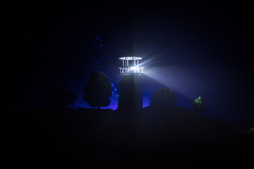 Lighthouse with light beam at night with fog. Old lighthouse standing on mountain. Table decoration. Toned background. Moonlighting.