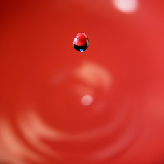 A water droplet falling into a bowl of water with a red background.