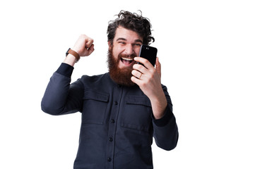 Portrait of a happy young bearded mann isolated over white background, holding mobile phone,...