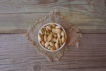Pistachios in a white bowl on a burlap atop an old wooden surface. Dieting concept. Fresh nuts. 