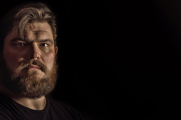 Obraz premium Close-up portrait strong serious brutal bearded man on black. Confident and dramatic concept
