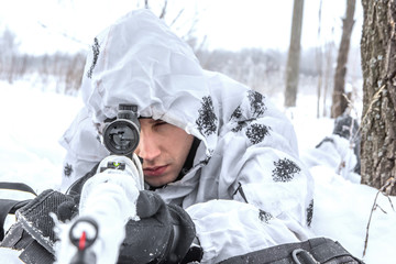 Fototapeta na wymiar Closeup portrait Man soldier in the winter on a hunt with a sniper rifle in white winter camouflage lying in the snow