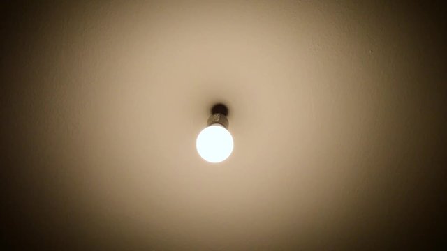 Bulb without lamp hanging from the ceiling moving while turning on and off. Lighting of an old and gloomy room.
