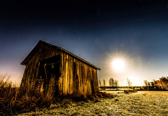 Full moon and stars shine over abandoned shed standing alone in the field, deep autumn, old grass freezing under cold clear skies at night - Powered by Adobe