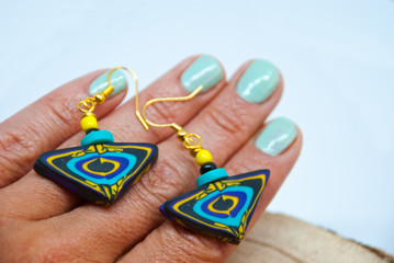 Stylish handmade earrings in boho style on hand with color nails. Tribal african jewelry background.