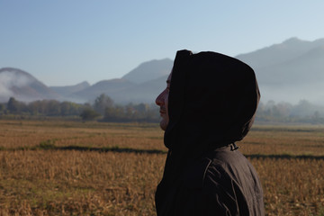 Profile close up portrait of Caucasian male traveller dressed in black jacket with hood, looking at distance, admiring nice scenery, breathing fresh morning air in mountains, enjoying nature alone.